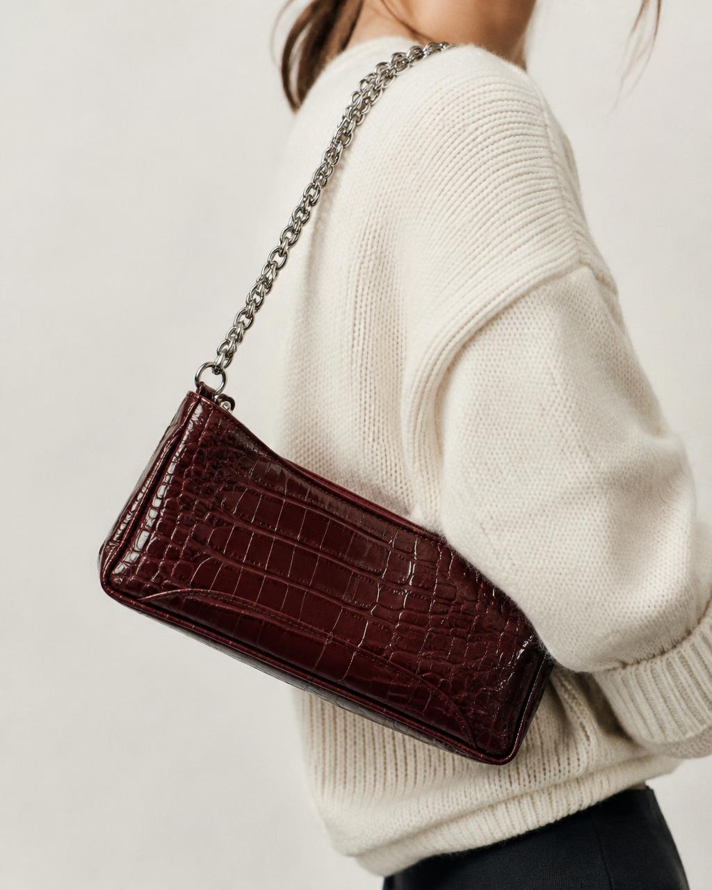 Burgundy croc-embossed shoulder bag worn over a cream knit