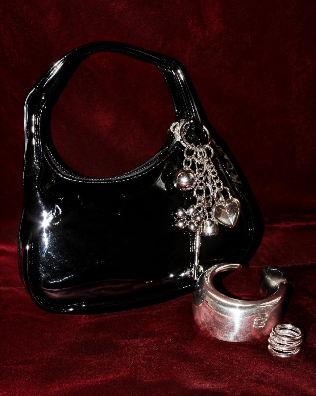 Black patent bag with silver charms and a cuff on burgundy velvet