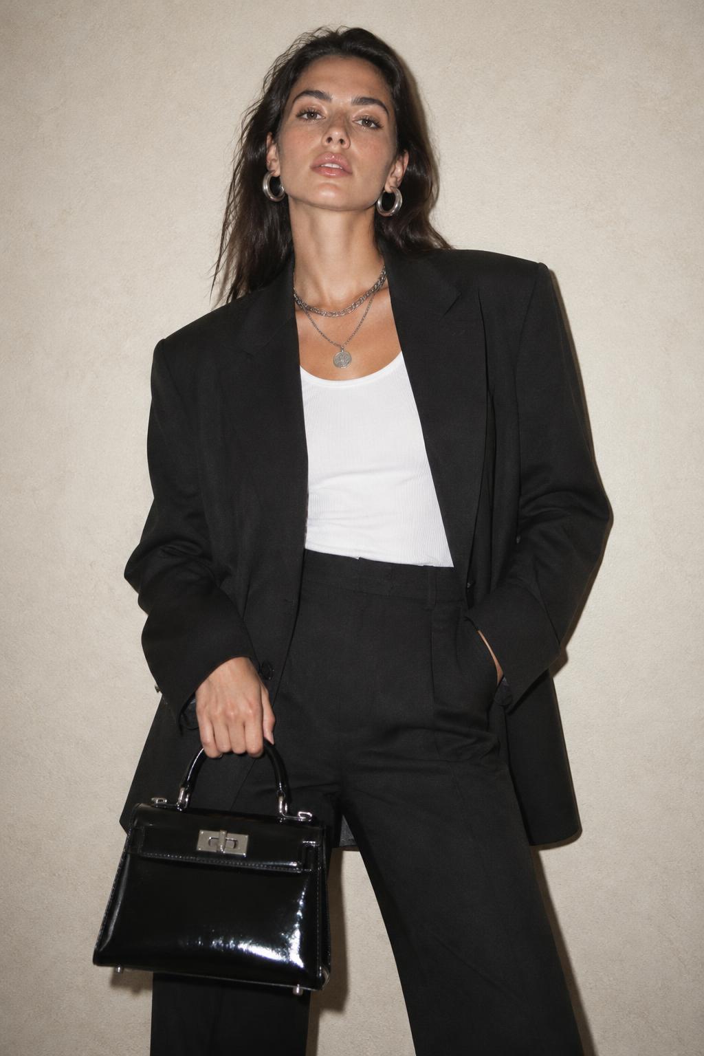 Model in a black blazer with silver hoops and a patent bag