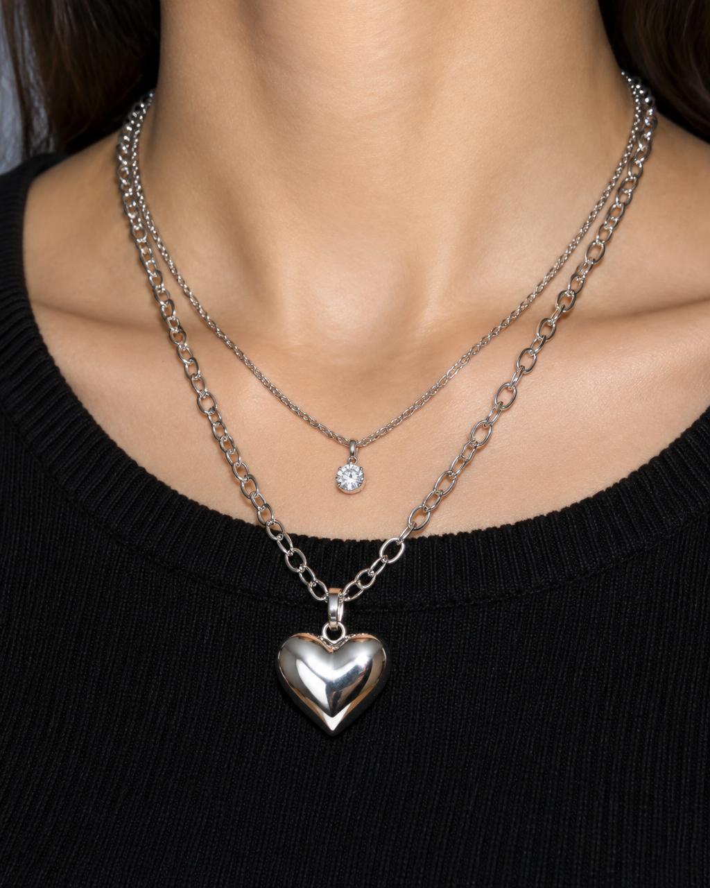 Layered silver chains with a puffy heart pendant over a black knit top