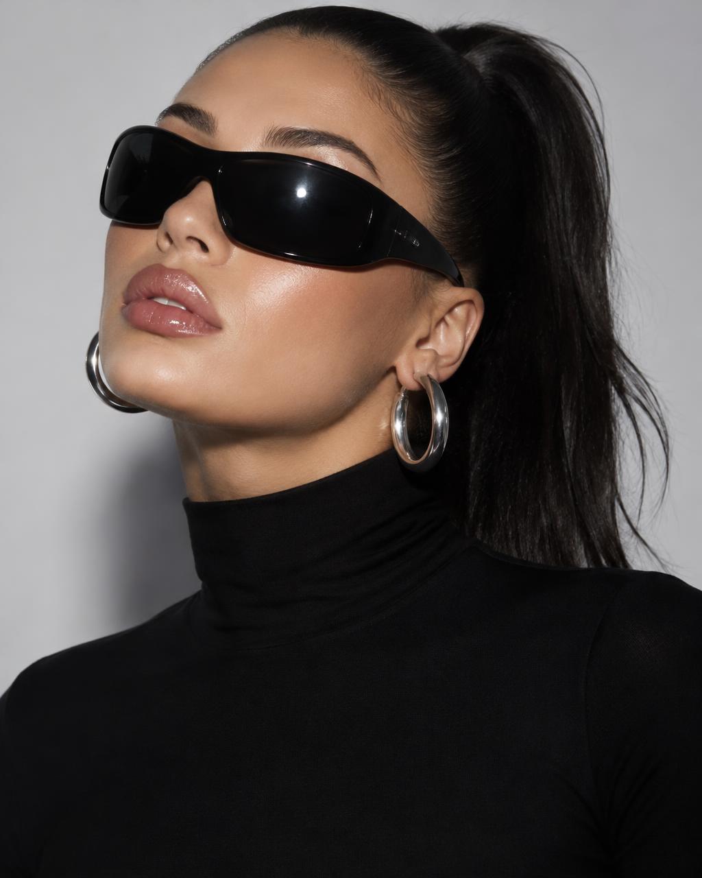 Model with a sleek high ponytail in black wraparound sunglasses and silver hoops