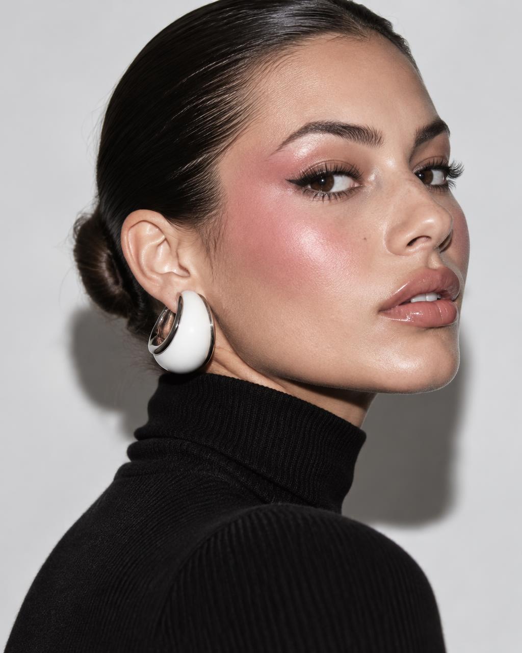 Model with a low bun and pink blush wearing a chunky white and silver sculptural hoop
